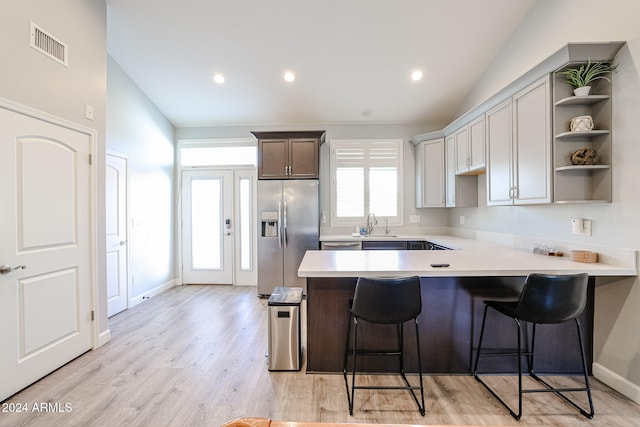 kitchen with kitchen peninsula, stainless steel appliances, lofted ceiling, light hardwood / wood-style floors, and a breakfast bar area