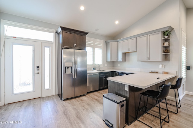 kitchen featuring lofted ceiling, a kitchen breakfast bar, light hardwood / wood-style flooring, kitchen peninsula, and stainless steel appliances