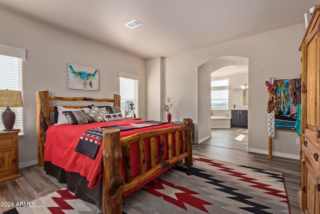 bedroom featuring multiple windows, ensuite bathroom, and dark wood-type flooring