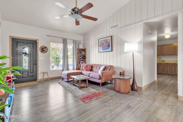 living room with wood walls, ceiling fan, light hardwood / wood-style floors, and vaulted ceiling