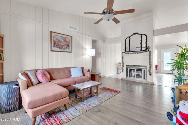 living room with hardwood / wood-style floors, ceiling fan, lofted ceiling, and wooden walls