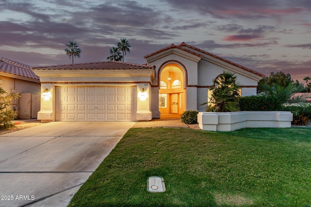 mediterranean / spanish-style home with a garage, concrete driveway, stucco siding, a tile roof, and a yard