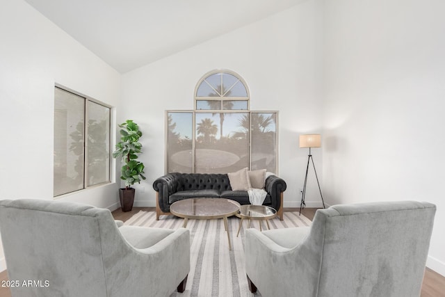 living room with wood finished floors, baseboards, and high vaulted ceiling