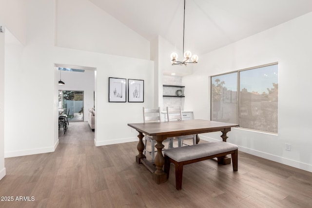 dining room with a chandelier, wood finished floors, baseboards, and high vaulted ceiling