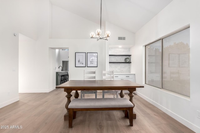 dining space with light wood-type flooring, high vaulted ceiling, a chandelier, and baseboards