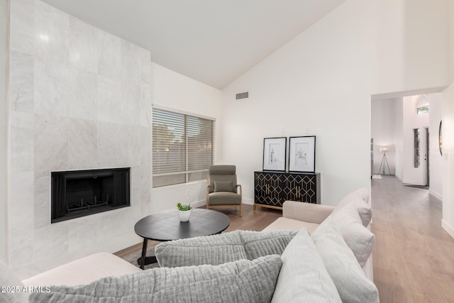 living area with high vaulted ceiling, baseboards, wood finished floors, and a tile fireplace