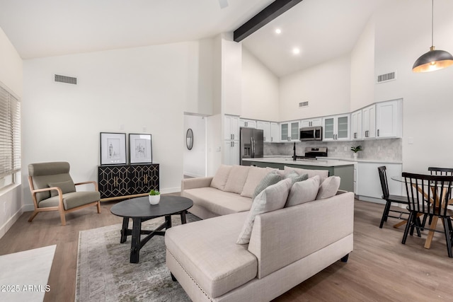living room featuring high vaulted ceiling, light wood finished floors, beamed ceiling, and baseboards