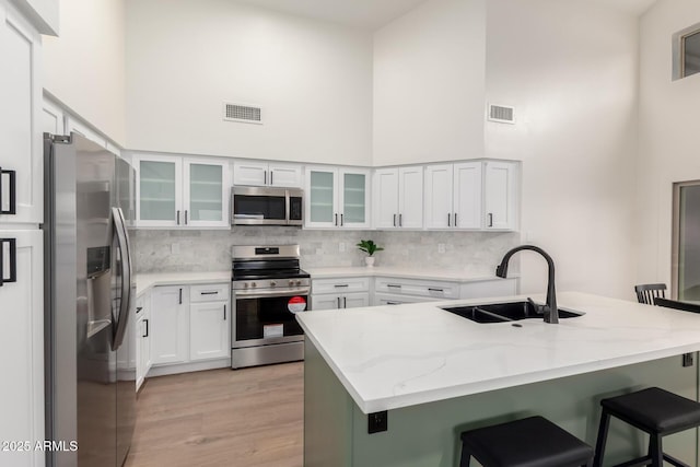 kitchen with stainless steel appliances, a towering ceiling, a sink, a breakfast bar, and backsplash