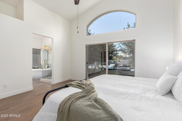 bedroom featuring access to exterior, a towering ceiling, wood finished floors, baseboards, and ensuite bathroom