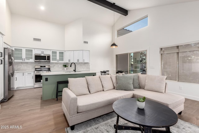living area featuring high vaulted ceiling, beam ceiling, and light wood finished floors