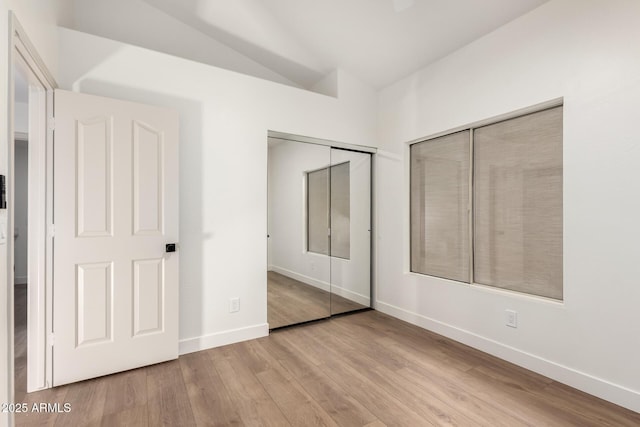 unfurnished bedroom with wood finished floors, baseboards, lofted ceiling, and a closet