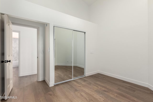 unfurnished bedroom with wood finished floors, baseboards, and a closet