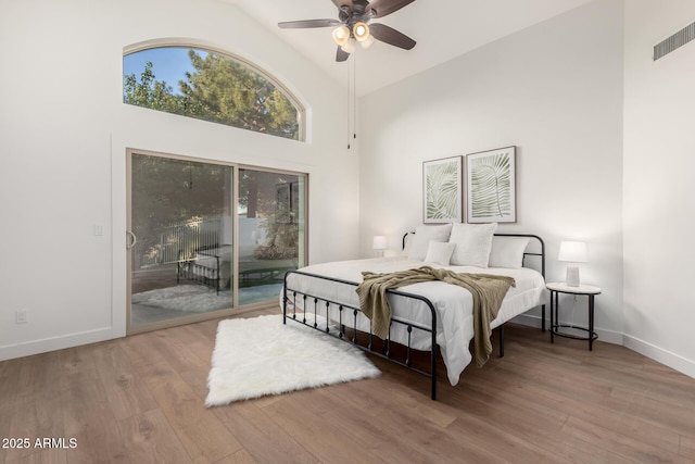 bedroom with access to outside, high vaulted ceiling, wood finished floors, and baseboards