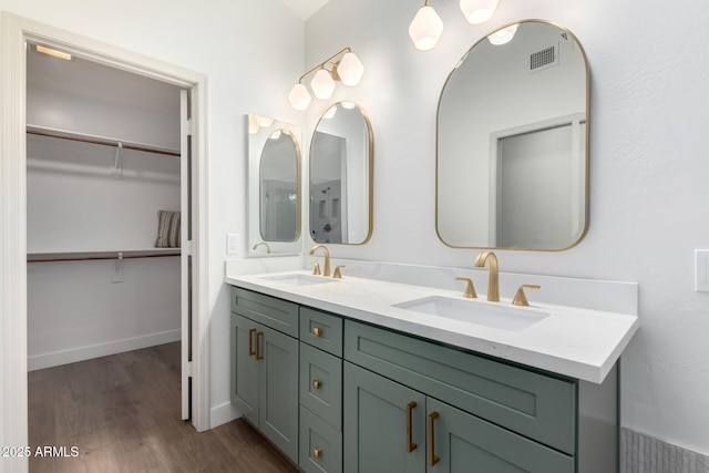 full bath with wood finished floors, double vanity, a walk in closet, and baseboards