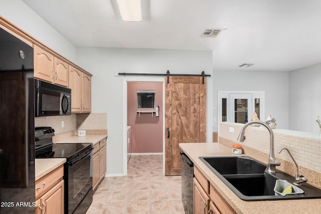 kitchen featuring sink, backsplash, black appliances, light brown cabinetry, and a barn door