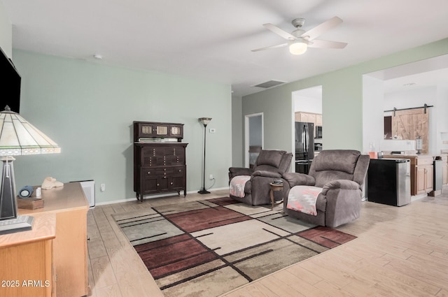 living room with ceiling fan, a barn door, and light hardwood / wood-style floors