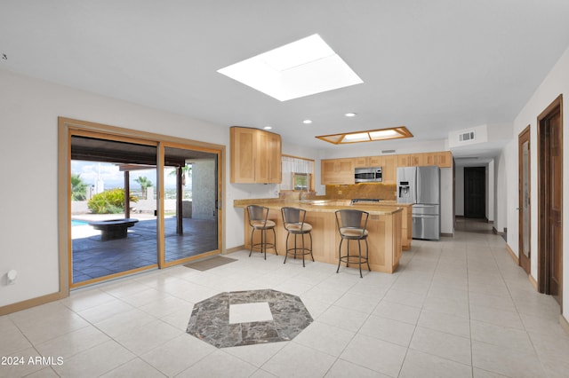 kitchen with a skylight, a kitchen bar, stainless steel appliances, kitchen peninsula, and decorative backsplash