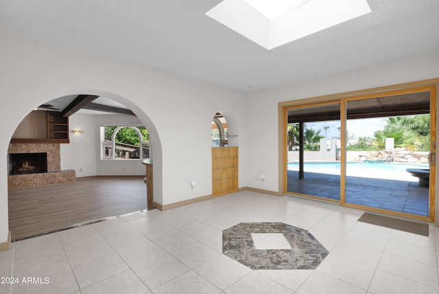 interior space with light tile patterned floors, beam ceiling, a skylight, and a fireplace