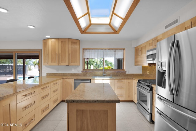 kitchen with appliances with stainless steel finishes, a healthy amount of sunlight, light stone counters, and a center island