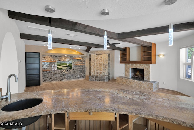 kitchen with a tiled fireplace, a textured ceiling, beamed ceiling, and a sink