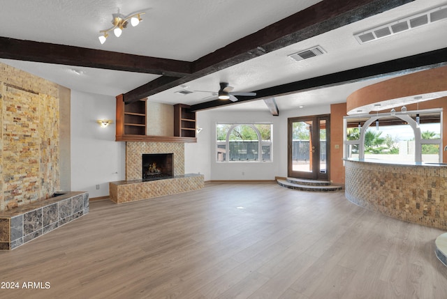 unfurnished living room with beamed ceiling, a textured ceiling, a tile fireplace, ceiling fan, and light hardwood / wood-style floors