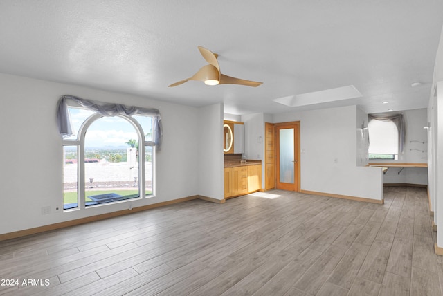 unfurnished living room featuring baseboards, a textured ceiling, ceiling fan, and light wood finished floors