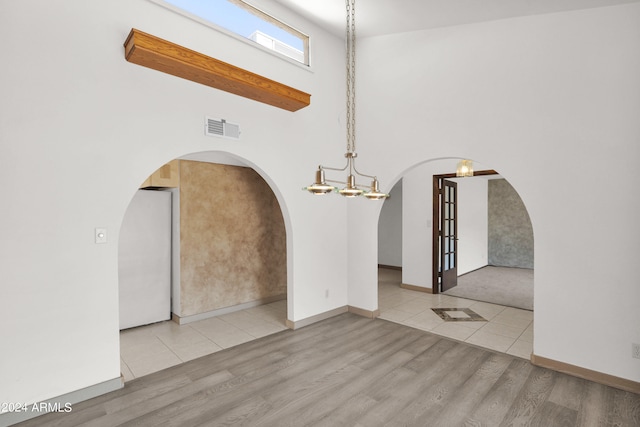 spare room with a towering ceiling, a notable chandelier, and light hardwood / wood-style floors