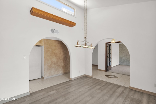 spare room with visible vents, baseboards, a towering ceiling, wood finished floors, and arched walkways