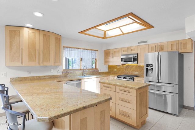 kitchen with a kitchen bar, stainless steel appliances, light brown cabinetry, light stone counters, and sink