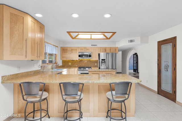 kitchen featuring a breakfast bar, kitchen peninsula, light brown cabinets, and appliances with stainless steel finishes