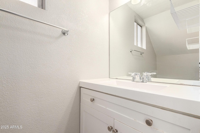 bathroom featuring vanity, lofted ceiling, and a textured wall