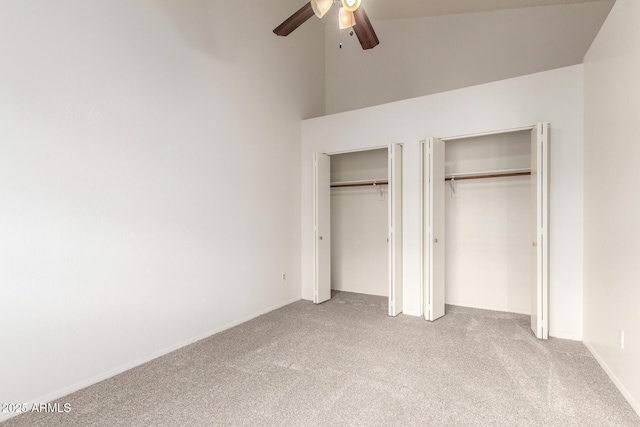 unfurnished bedroom featuring vaulted ceiling, carpet flooring, a ceiling fan, and two closets