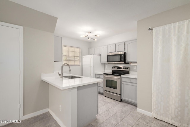 kitchen with baseboards, a peninsula, a sink, light countertops, and appliances with stainless steel finishes