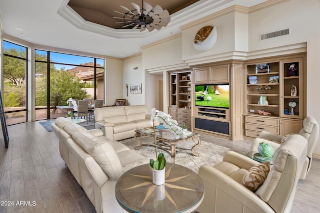 living room featuring light hardwood / wood-style floors, a high ceiling, a wall of windows, a tray ceiling, and ornamental molding