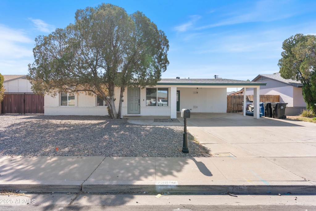 ranch-style house featuring an attached carport, concrete driveway, and fence