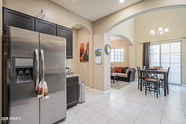 kitchen featuring stainless steel fridge with ice dispenser, arched walkways, light tile patterned flooring, a chandelier, and baseboards