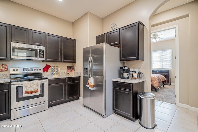 kitchen featuring stainless steel appliances, light tile patterned floors, arched walkways, and light stone counters