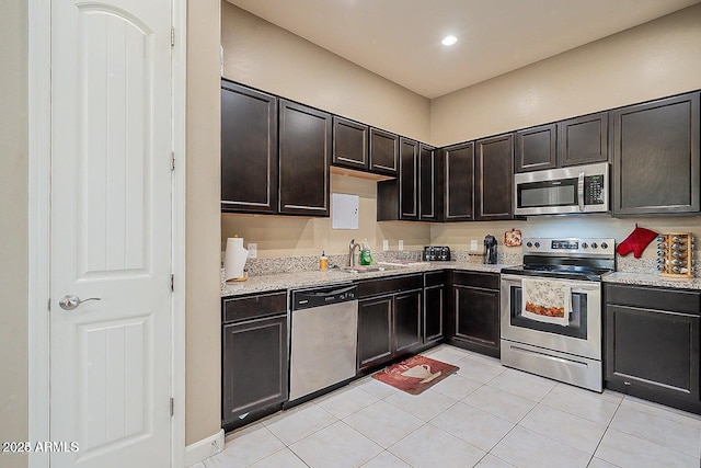 kitchen with stainless steel appliances, light tile patterned floors, a sink, recessed lighting, and light stone countertops