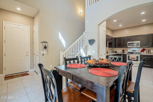 dining area with light tile patterned floors, arched walkways, stairs, recessed lighting, and a towering ceiling