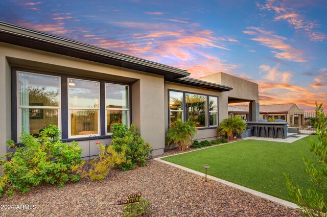 back house at dusk with exterior bar, a lawn, and a patio area