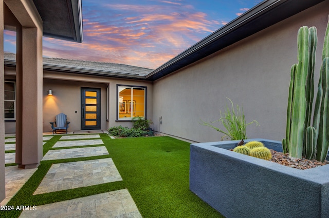 exterior entry at dusk with a patio and a lawn