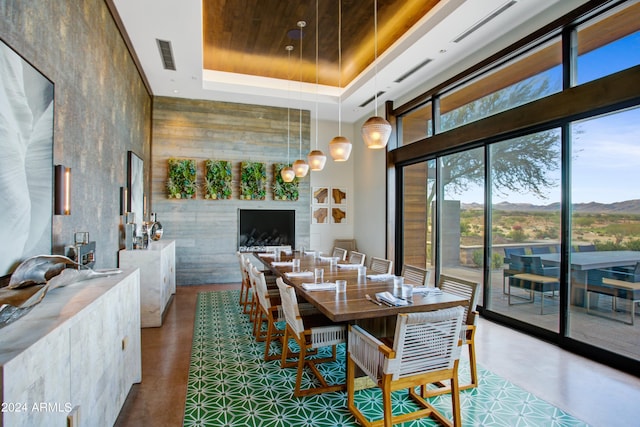 dining area with a mountain view, a towering ceiling, a raised ceiling, a large fireplace, and concrete flooring