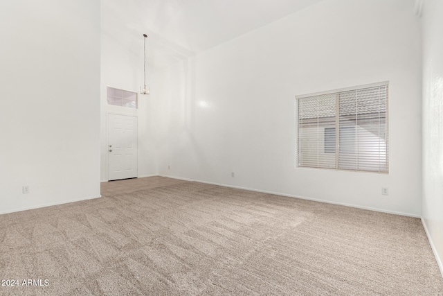 spare room with carpet floors, an inviting chandelier, and high vaulted ceiling