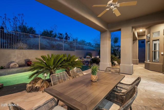 patio at night with ceiling fan, outdoor dining space, and fence