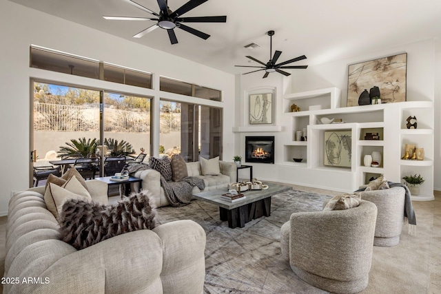 living room with built in features, visible vents, ceiling fan, and a glass covered fireplace