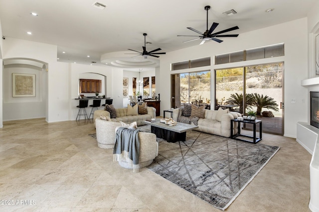 living area with arched walkways, visible vents, a ceiling fan, and a glass covered fireplace