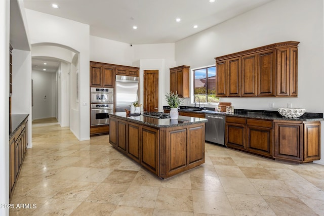 kitchen featuring a kitchen island, dark stone countertops, arched walkways, stainless steel appliances, and a sink