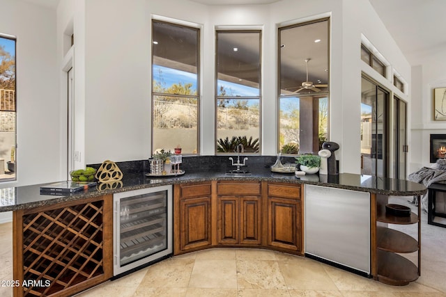 bar with beverage cooler, a ceiling fan, a sink, stone tile floors, and wet bar