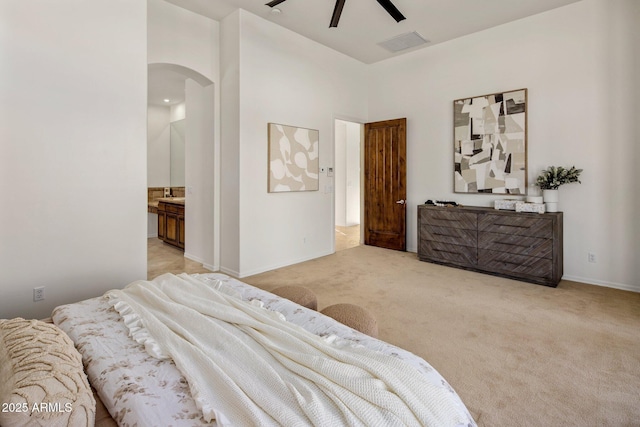 bedroom with visible vents, ensuite bath, arched walkways, a towering ceiling, and light colored carpet