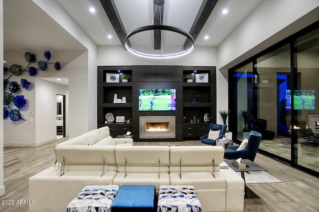 living area featuring built in features, a fireplace, wood finished floors, baseboards, and beamed ceiling